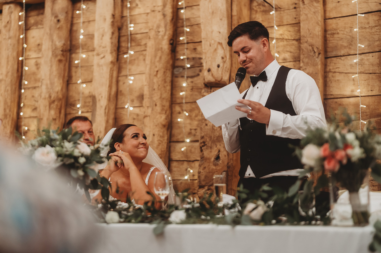 A best man giving a speech while the bride laughs at the top table