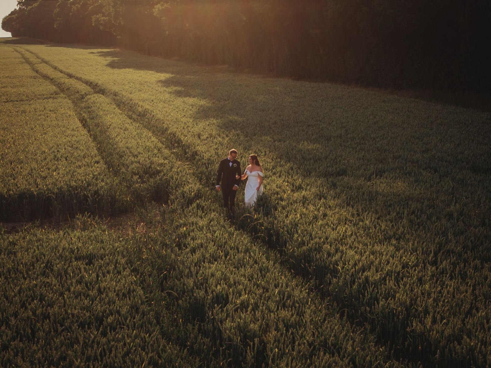 documentary wedding photography — drone view of couple walking through a wheat field at golden hour