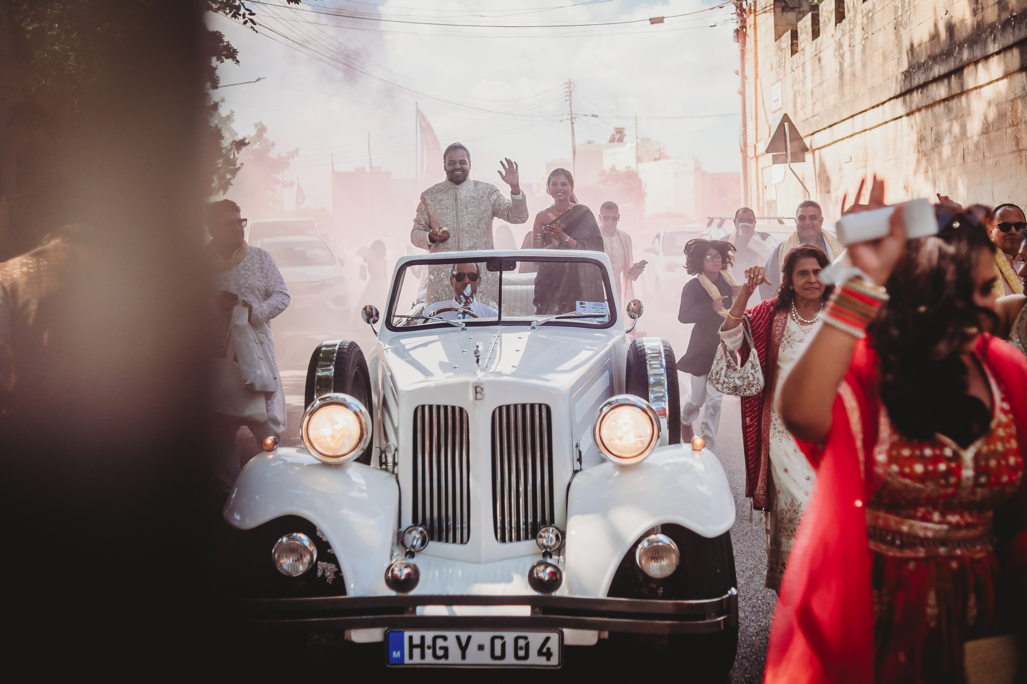 Lakshna & Neil / Villa Bologna Wedding 8 Baraat with blue smoke flares in a closed street in Attard, Malta — groom arriving by vintage car