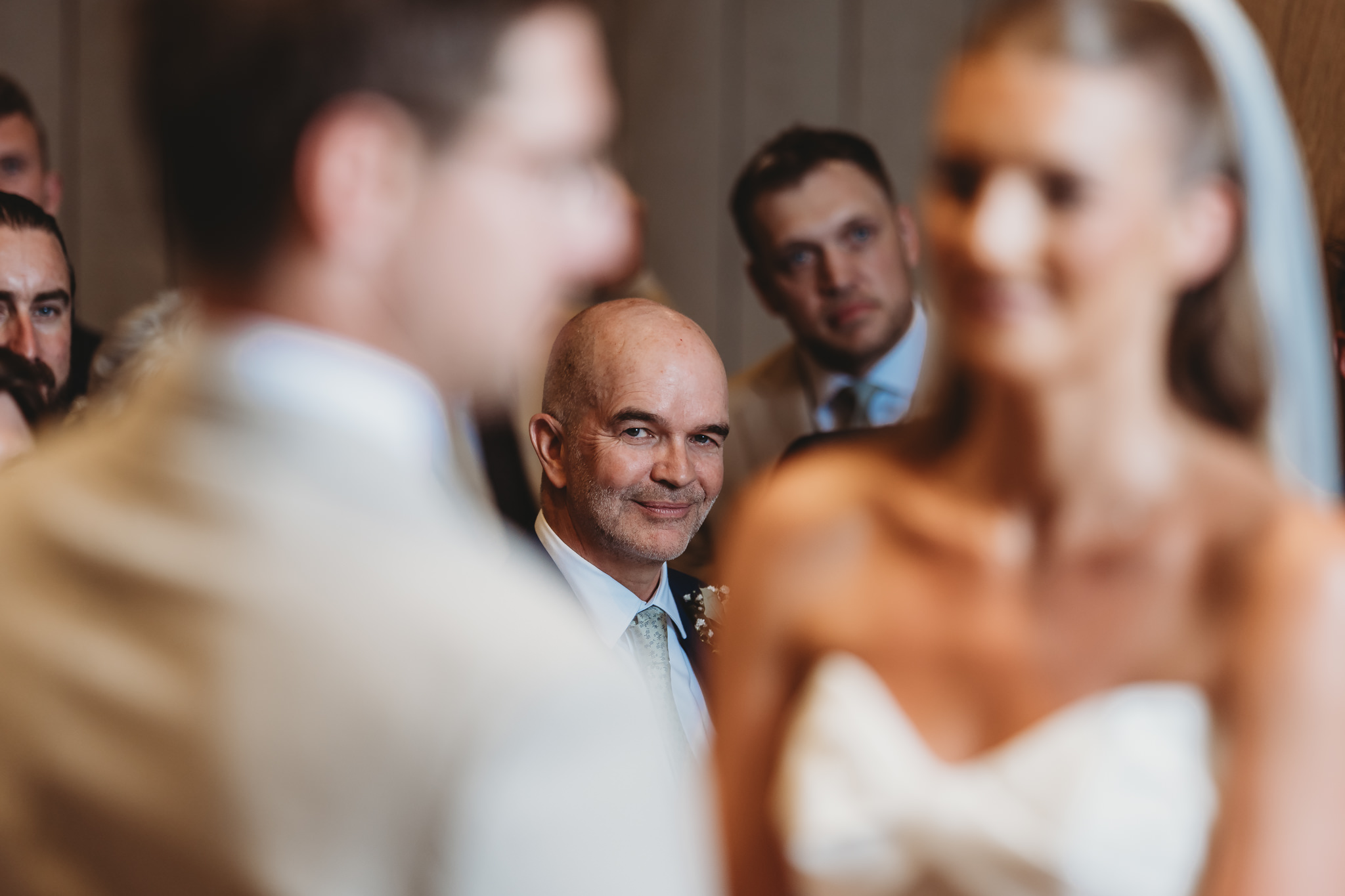Father of the bride watching the ceremony, framed in the gap between the bride and groom