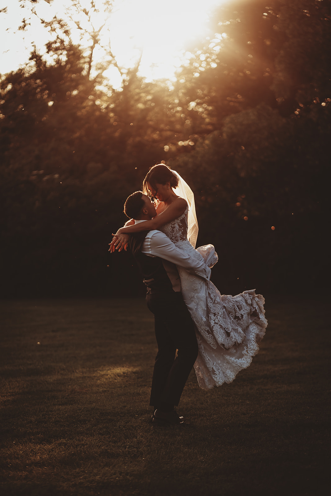 documentary wedding photography — groom lifting the bride into a kiss at sunset at Apton Hall, Essex