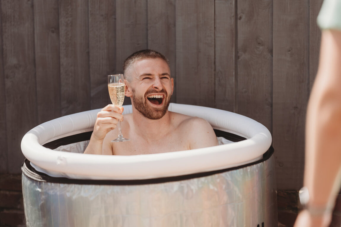 Groom laughing in an ice bath with a drink on his wedding morning