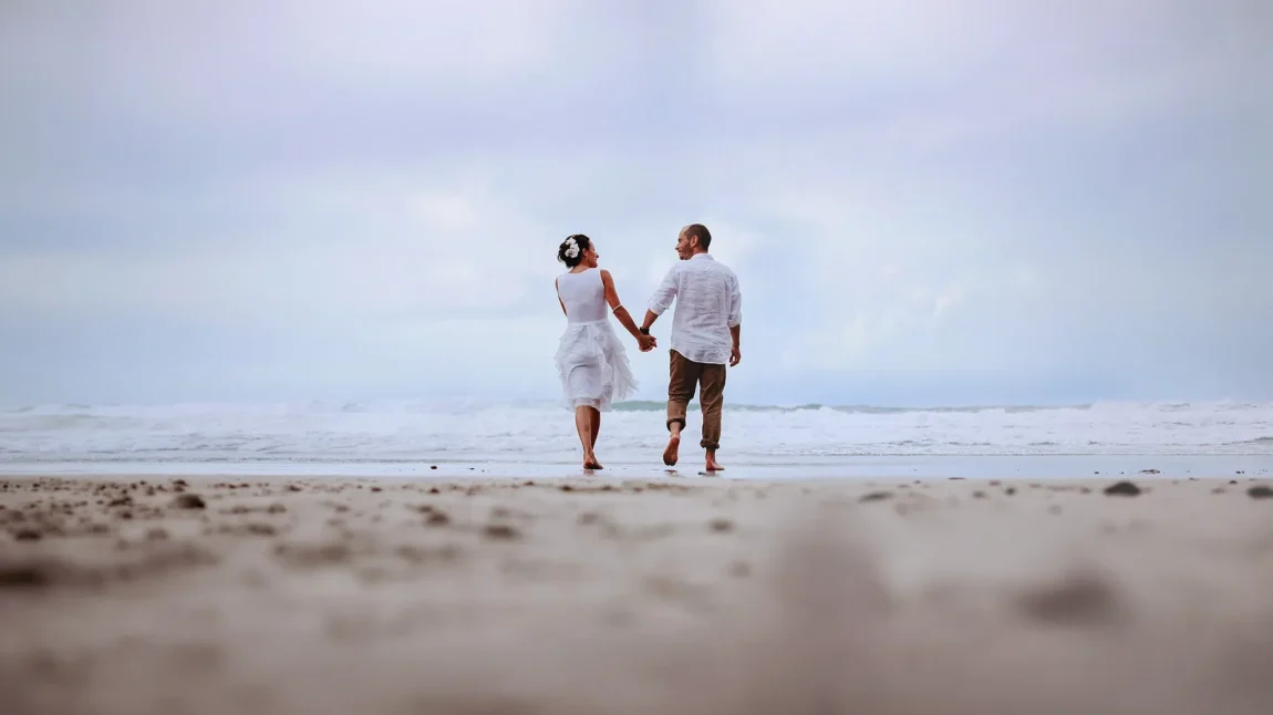 Bride and groom walking barefoot hand in hand along the shoreline, beach wedding photography by Matt Wing