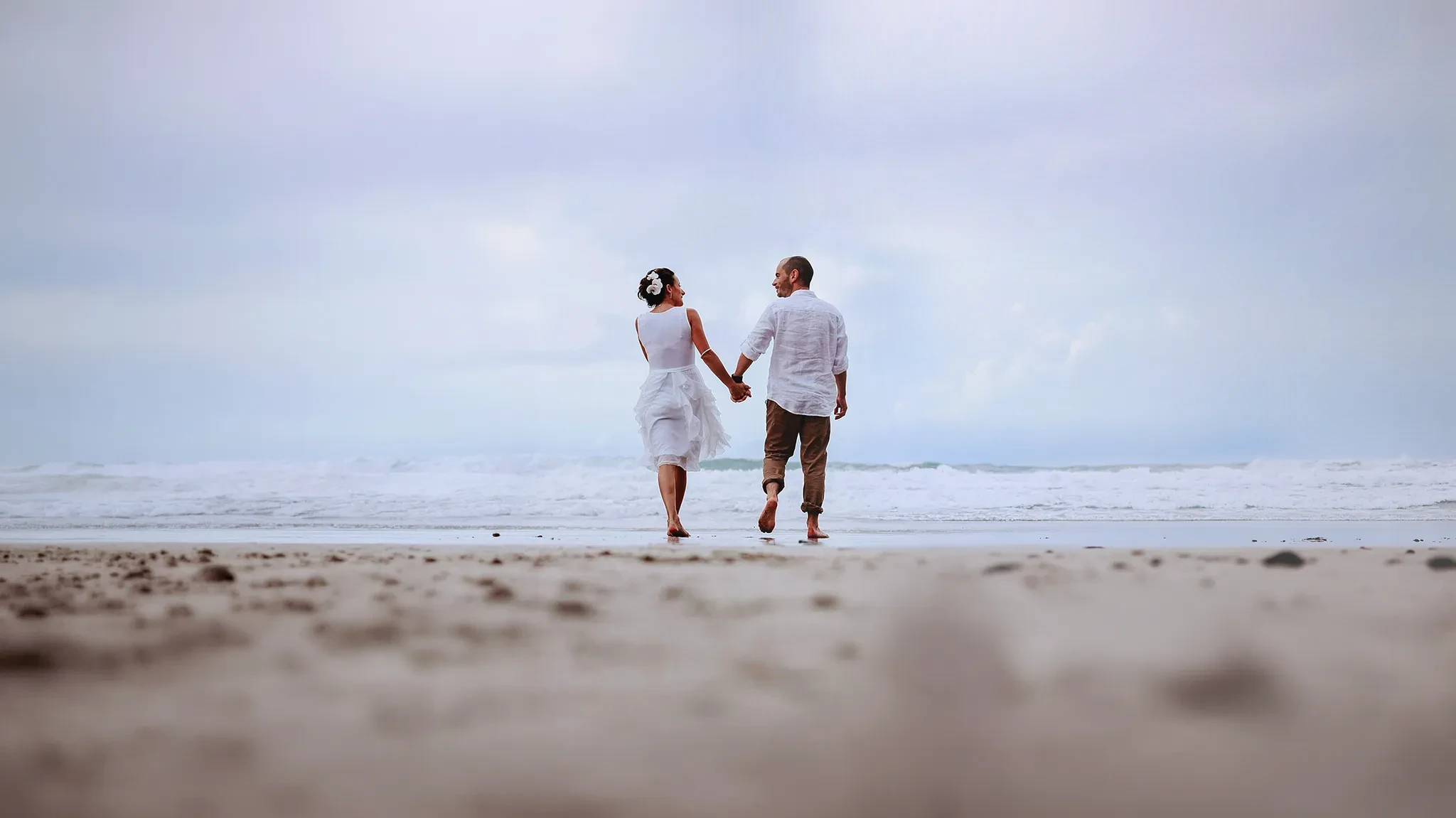 Cornwall beach wedding photographer Matt Wing: bride and groom walking barefoot hand in hand along the shoreline