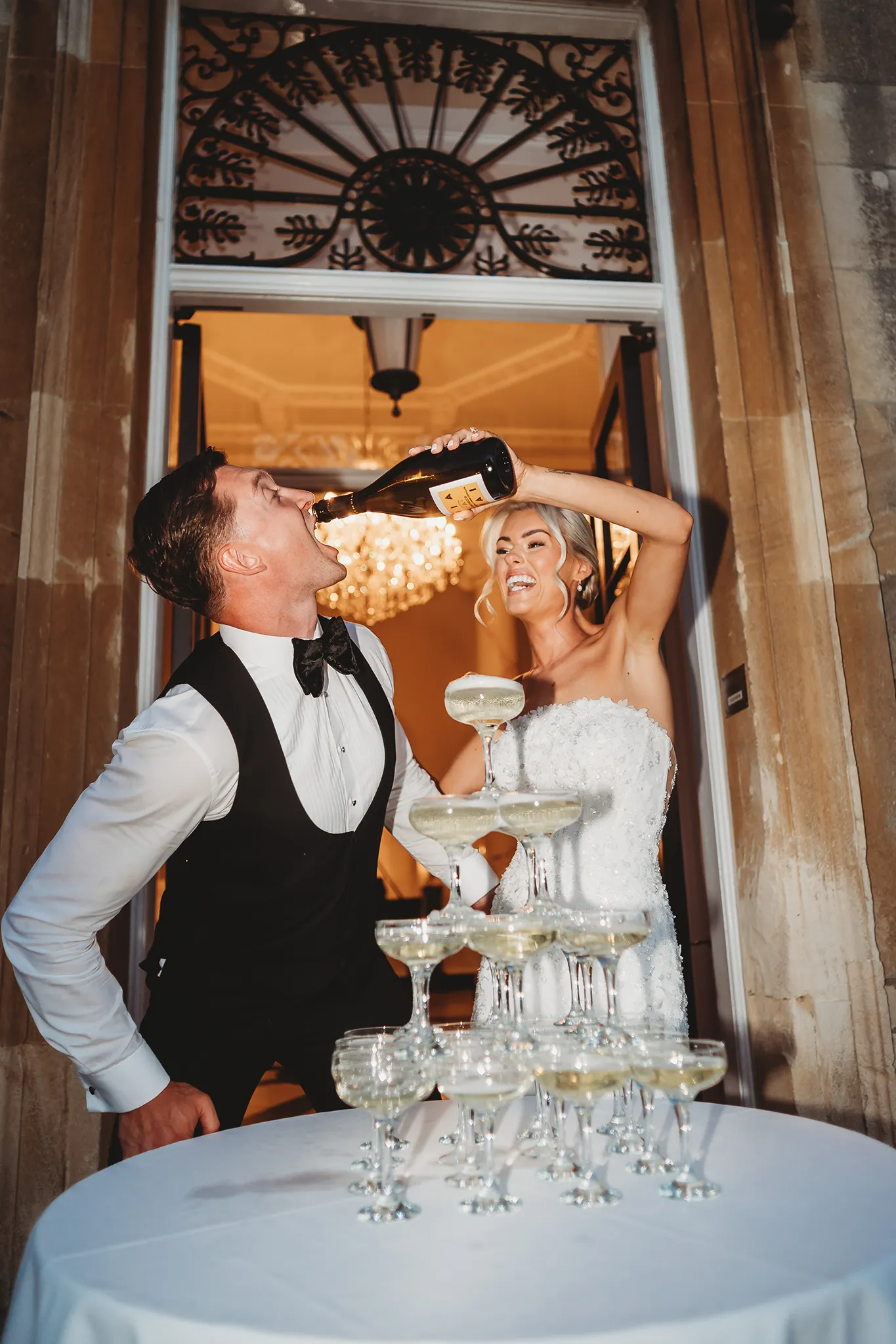 documentary wedding photography at Botleys Mansion — groom drinking from the bottle beside the champagne tower