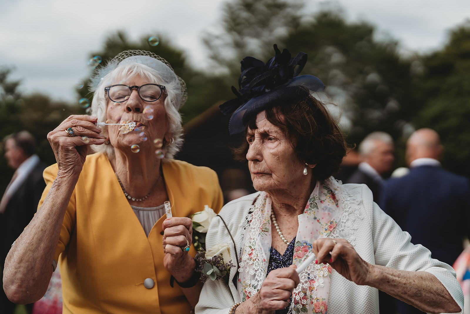 Two grandmothers concentrating hard on blowing bubbles at a wedding, unposed documentary photograph