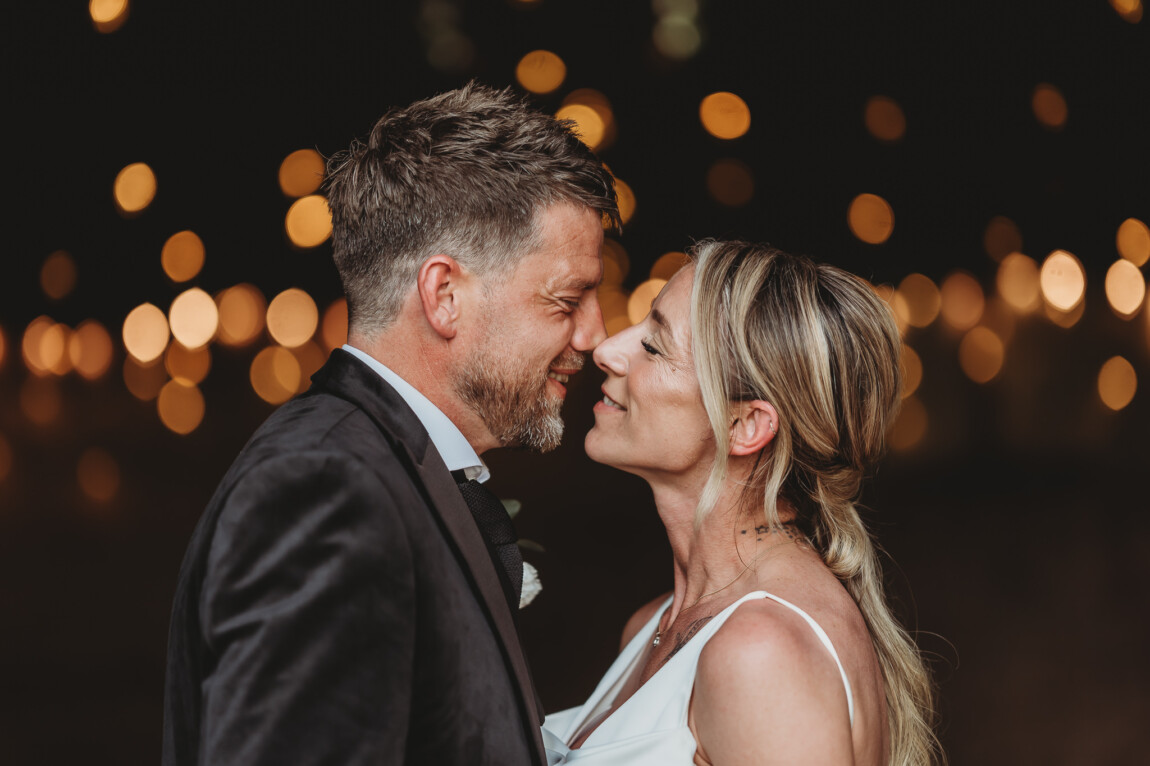 Laura and Liam nose to nose under festoon lights on their wedding night at The Green, Cornwall