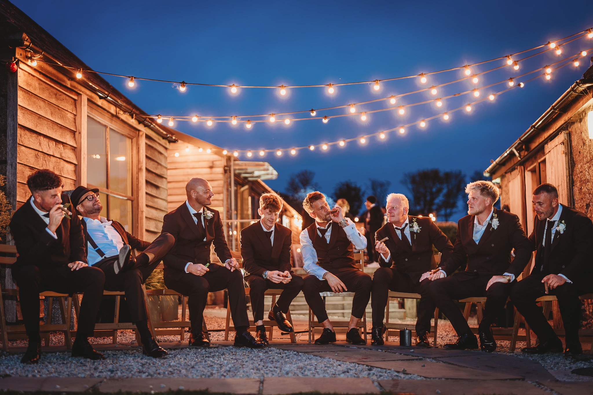 Wedding guests sitting outside under festoon lights at blue hour, The Green Cornwall