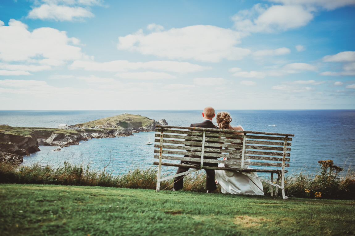 Cornwall beach wedding: bride and groom on a bench on the Headland above Newquay, looking out to sea