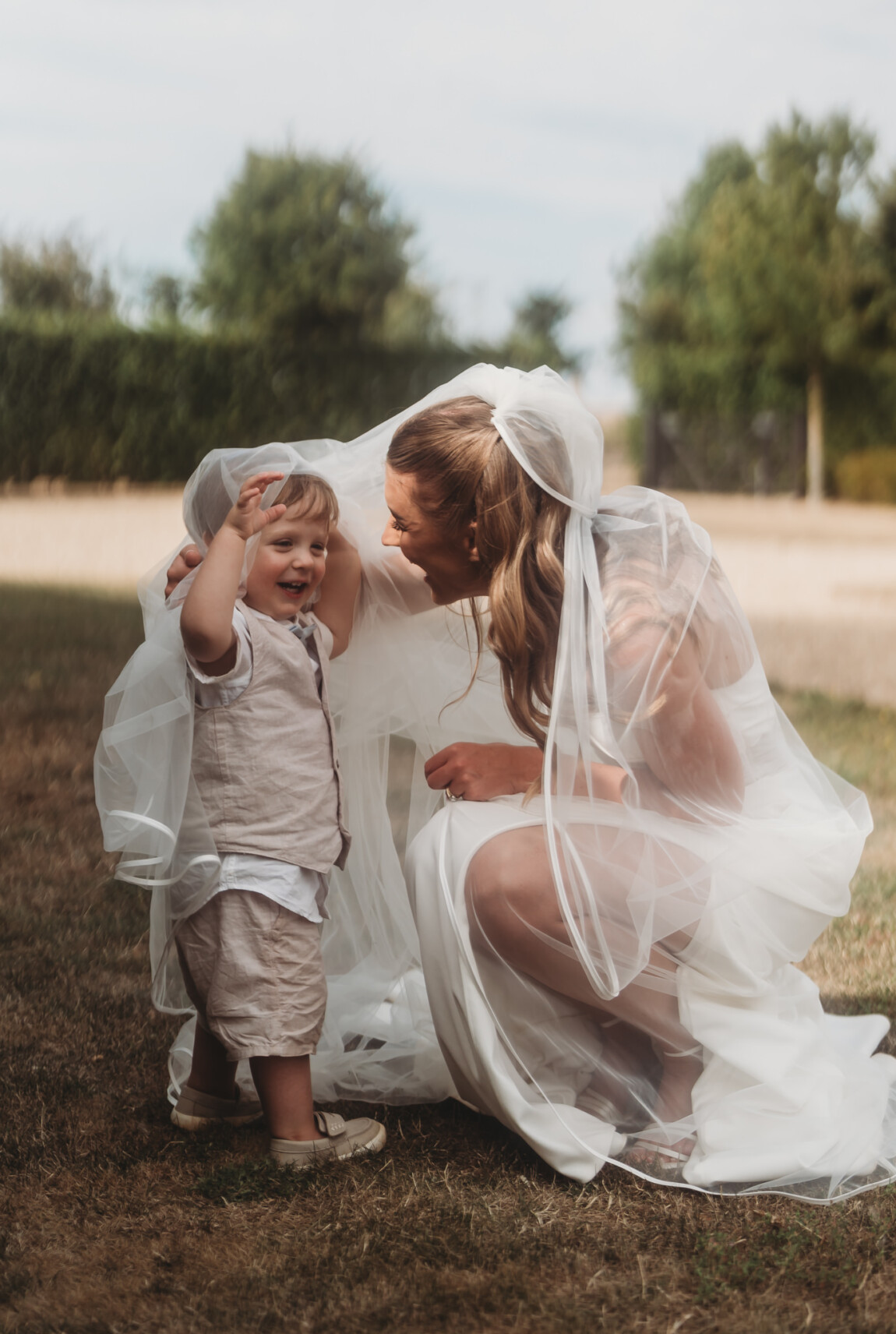 Bride hugging a page boy under her veil, documentary wedding photography by Matt Wing