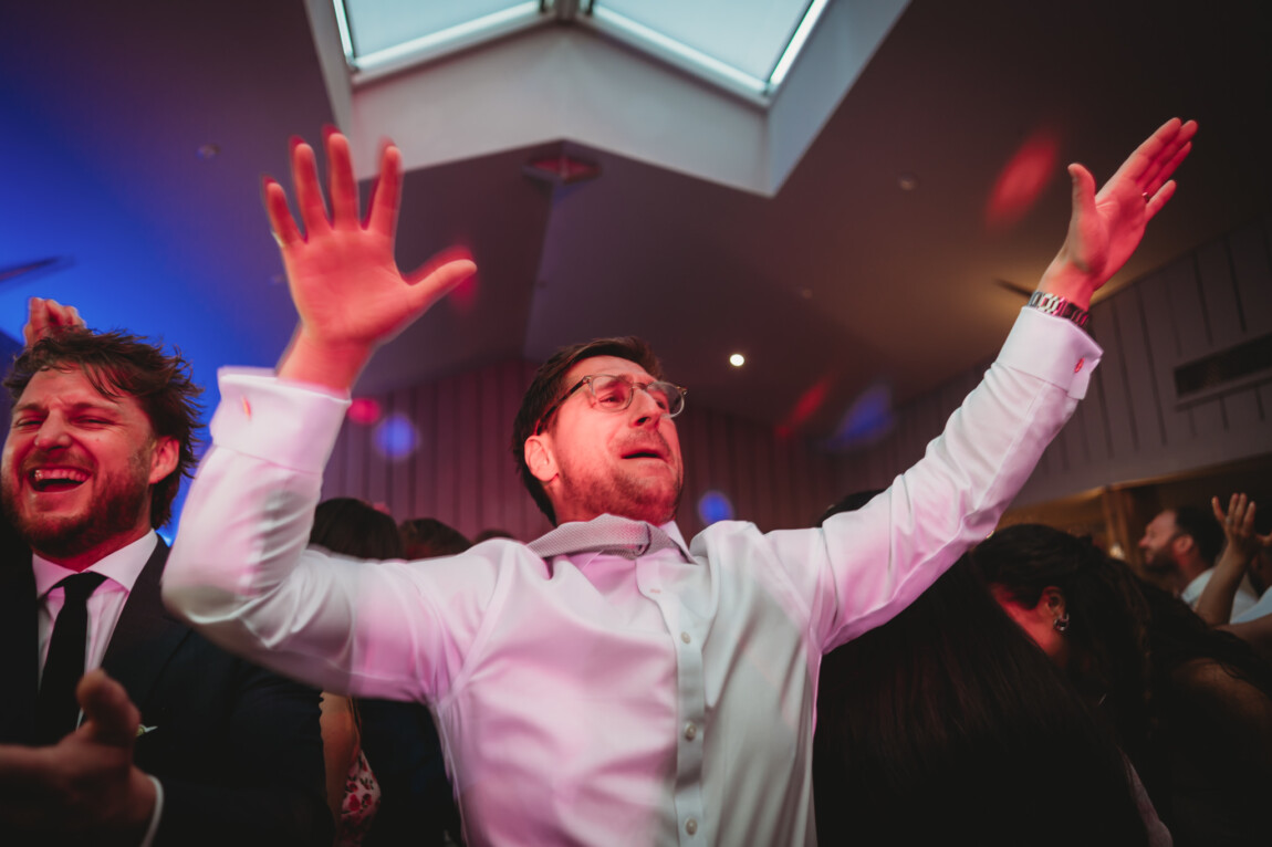 Groom with his arms in the air on the dancefloor, documentary wedding photography by Matt Wing