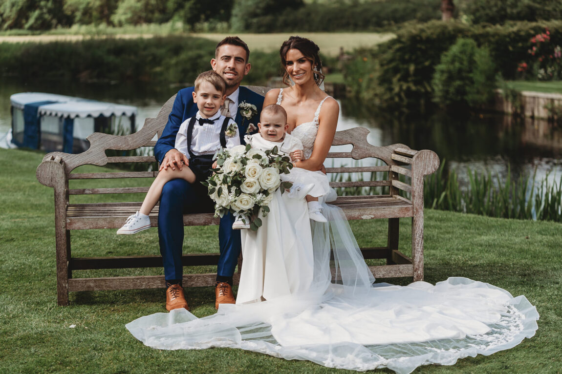 Bride and groom with the children on the bench by the River Stour at Le Talbooth
