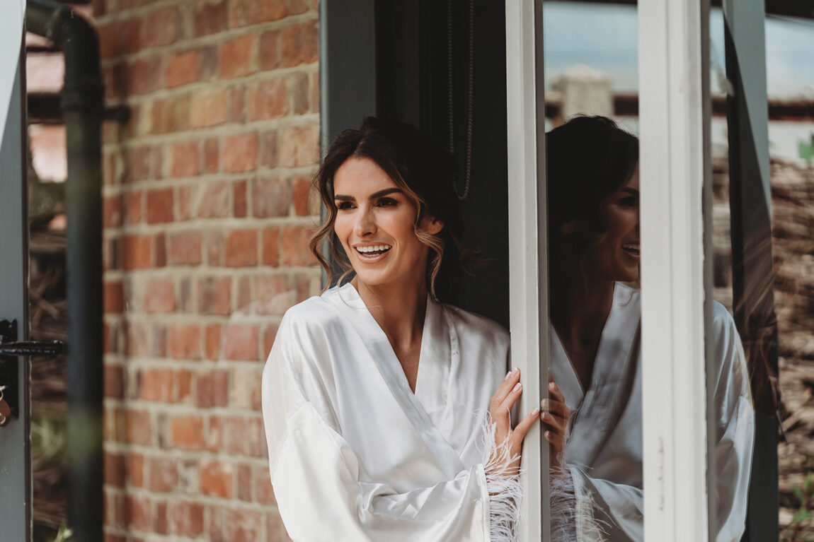 Bride laughing at the window in her robe on the wedding morning