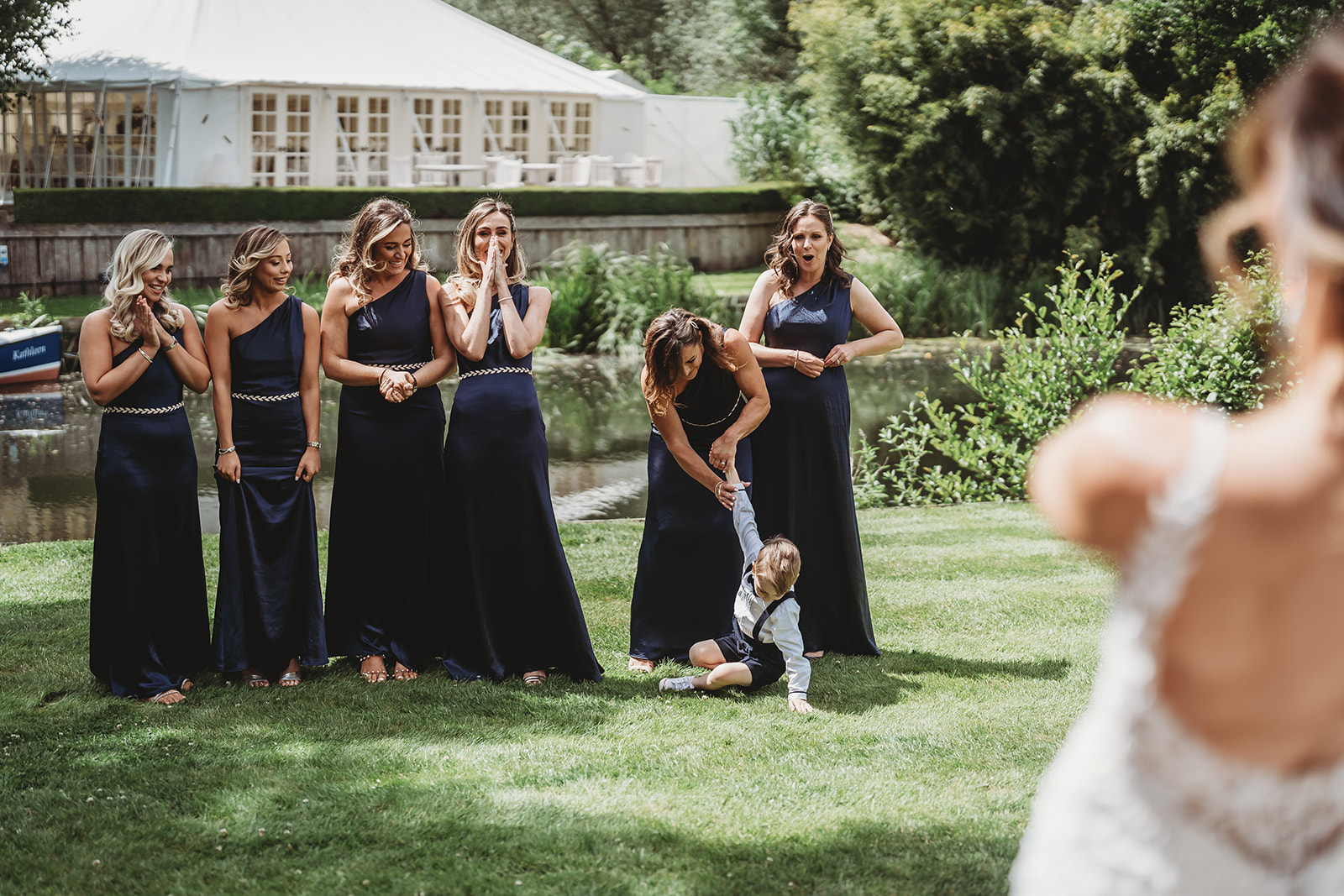 Bridesmaids reacting on the lawn by the river and the marquee at Le Talbooth