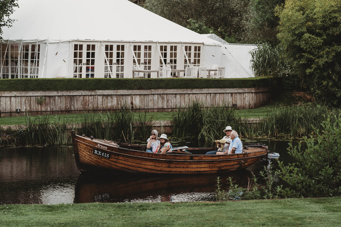Guests in a wooden boat on the River Stour beside the wedding marquee at Le Talbooth