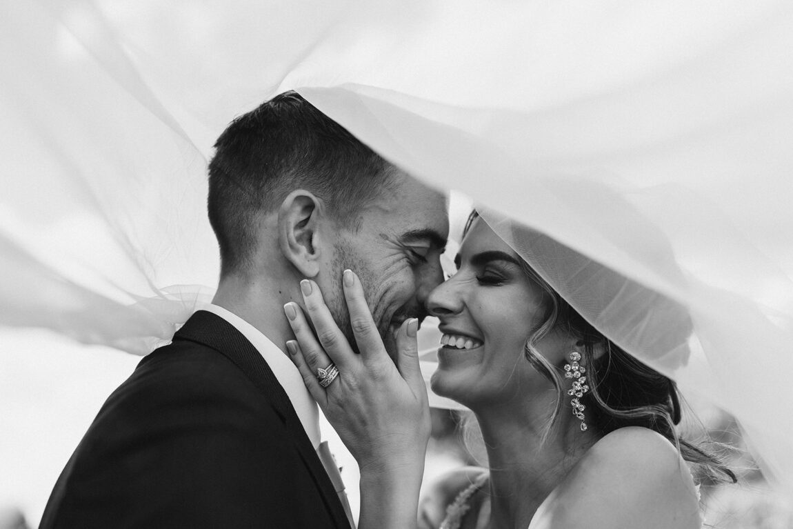 Black and white of the couple laughing beneath the veil