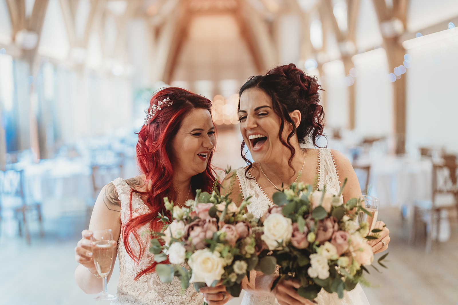 Two brides laughing together inside the oak barn at The Mill Barns