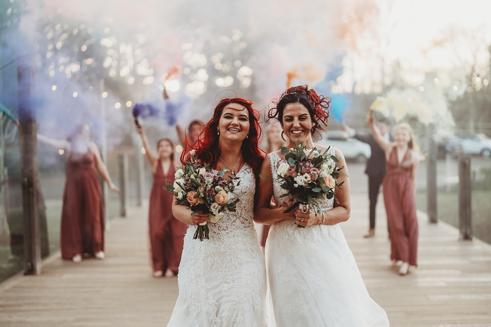 Two brides and their bridesmaids on the walkway with coloured smoke at The Mill Barns, Alveley