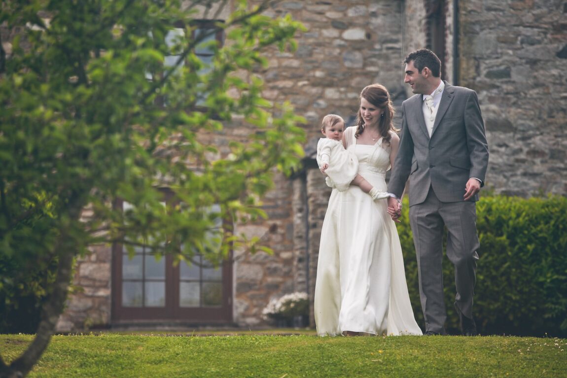 Bride and groom walking with their baby in the garden at Trevenna