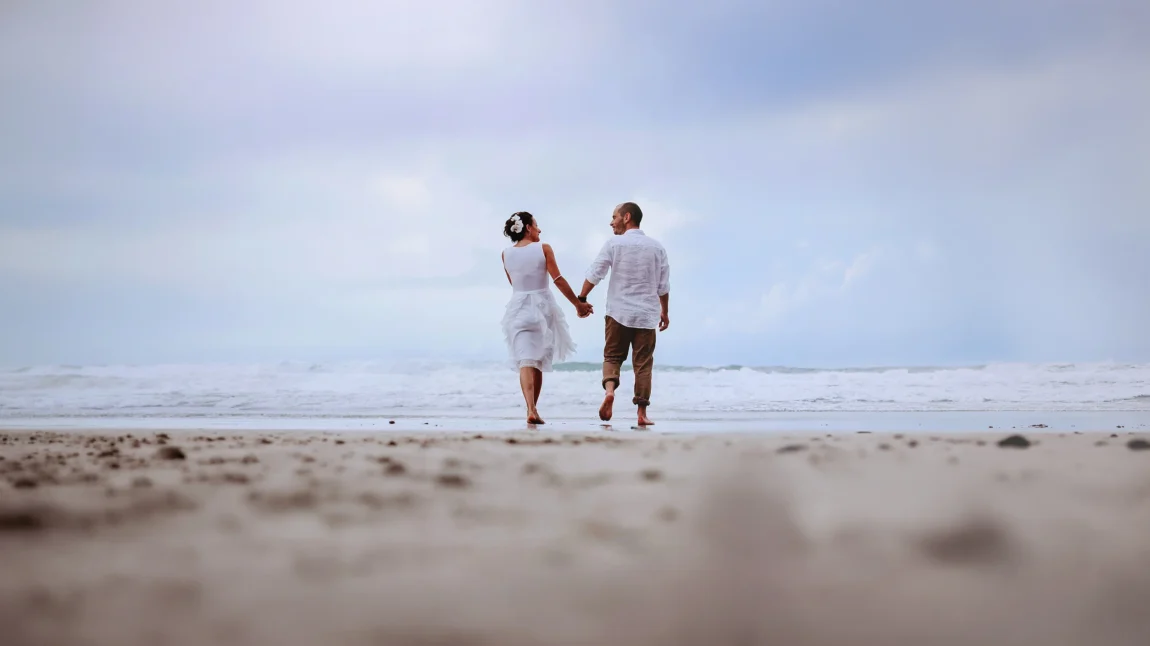 Couple walking hand in hand along the shoreline on their wedding day